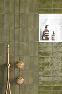 Aan deze douche muur werden mos groene wandtegels bejmat 5x15cm mat en blinkend gecombineerd. De douche werd afgewerkt met een wit marmer nis en gouden kranen.