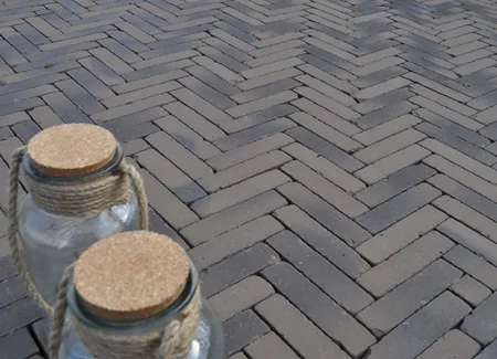 Detail van genuanceerde kleiklinkers in visgraatverband. Dit klassieke legpatroon zorgt voor extra stabiliteit en een levendig lijnenspel. De bruin zwarte klinkers geven een warme, tijdloze uitstraling aan oprit of terras. Inspiratie en advies bij Top Tegel 04 in Ieper, West-Vlaanderen.