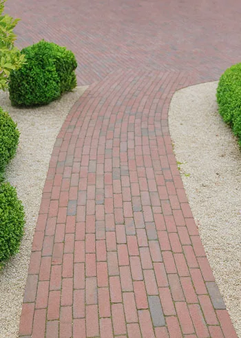 Sierlijk tuinpad aangelegd met rode kleiklinkers die zorgen voor een warme, natuurlijke uitstraling in de tuin. Deze gebakken klinkers zijn kleurvast, slijtvast en duurzaam, ideaal voor tuinpaden die intensief gebruikt worden. Inspiratie en advies bij Top Tegel 04 in Ieper, West-Vlaanderen.