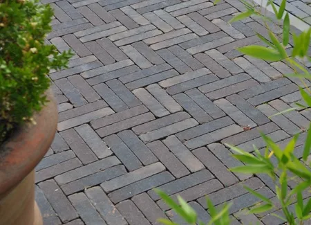 Detail van kleiklinkers in dubbel visgraatverband met warme, genuanceerde tinten. Dit legpatroon zorgt voor extra stabiliteit en een rijke, tijdloze uitstraling in tuin of terras. Duurzame, kleurvaste gebakken klinkers te ontdekken bij Top Tegel 04 in Ieper, West-Vlaanderen.